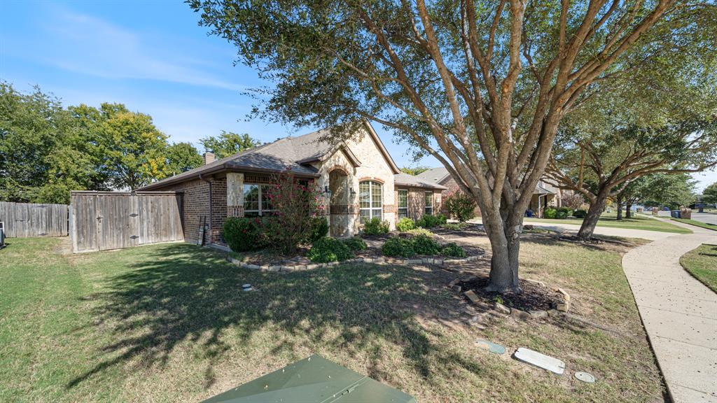 Brick exterior featuring a stone-accented arched entryway, mature shade trees, and wood-panel privacy fencing Brick exterior featuring a stone-accented arched entryway, mature shade trees, and wood-panel privacy fencing