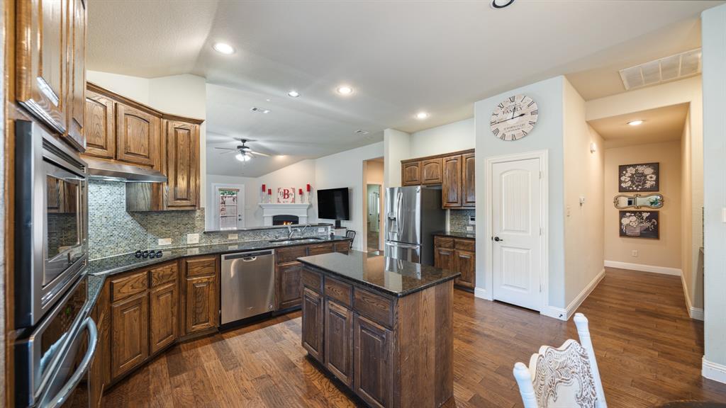 Kitchen featuring wood cabinetry, stone countertops, stainless steel appliances, a center island, and wood-finish flooring