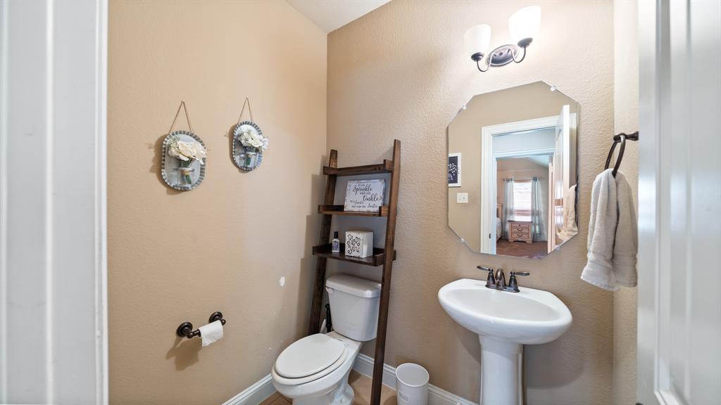 Powder room featuring a white porcelain pedestal sink with bronze-finish faucet, an octagonal wall mirror, and dual-light vanity fixture