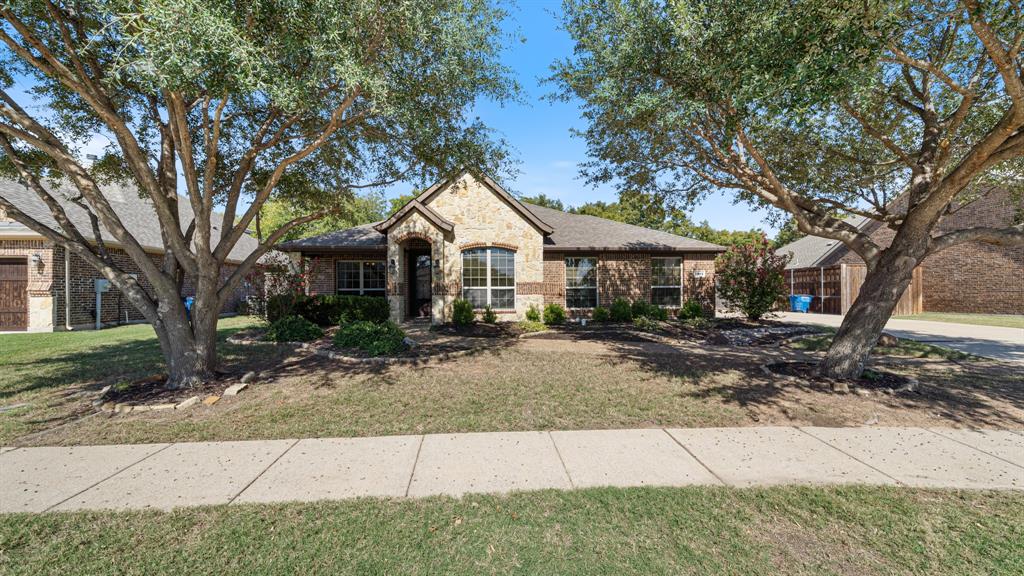 Single-story residence featuring a masonry exterior, multi-gable roofline, front-facing arched window, covered entryway, and mature shade trees Single-story residence featuring a masonry exterior, multi-gable roofline, front-facing arched window, covered entryway, and mature shade trees
