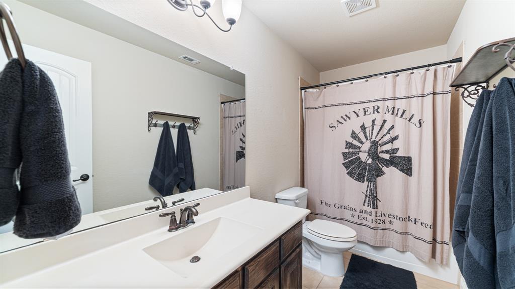 Bathroom featuring a vanity with an integrated sink, dark-toned cabinetry, a wide wall-mounted mirror, and a wall-mounted light fixture