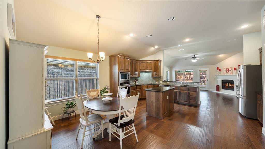 Kitchen featuring wood cabinetry, an island with stone countertops, built-in stainless steel appliances, wood-finish flooring, and a vaulted ceiling