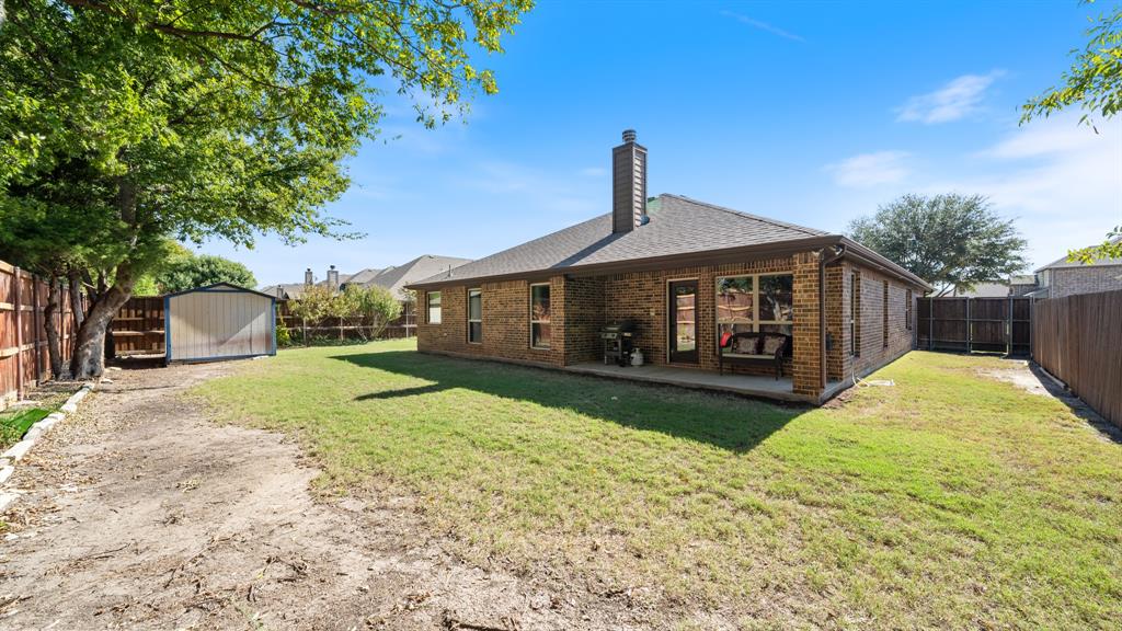 Backyard featuring a brick exterior, covered patio, masonry chimney, perimeter wood fencing, and a detached metal storage structure