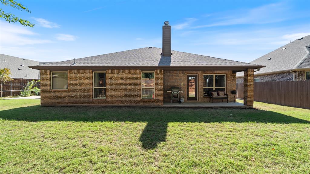 Rear exterior featuring brick siding, a covered concrete patio, a chimney, and a fenced backyard