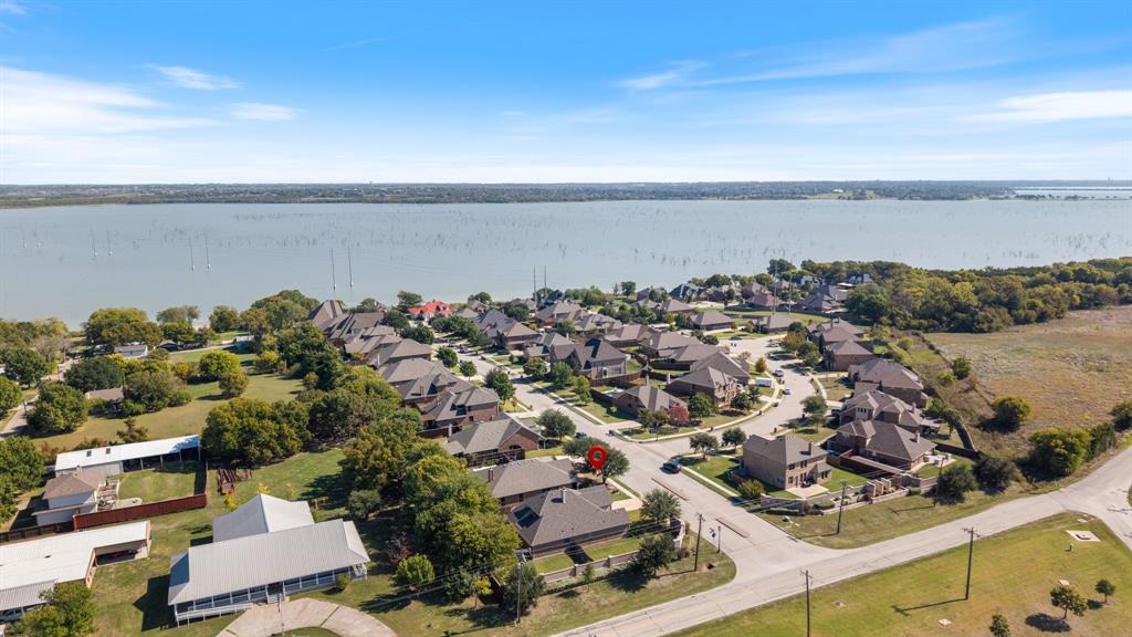 Aerial perspective of a residential neighborhood featuring waterfront positioning, expansive open water, mature tree coverage, and paved street access
