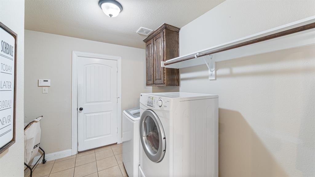 Laundry area featuring ceramic tile flooring, upper wood cabinetry, and a wall-mounted shelving unit with an integrated hanging rod