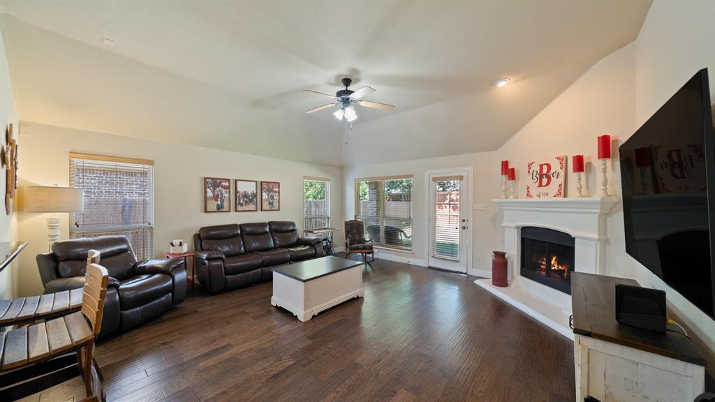 Living area featuring vaulted ceilings, wood-finish flooring, a fireplace with a decorative mantel, and a ceiling fan