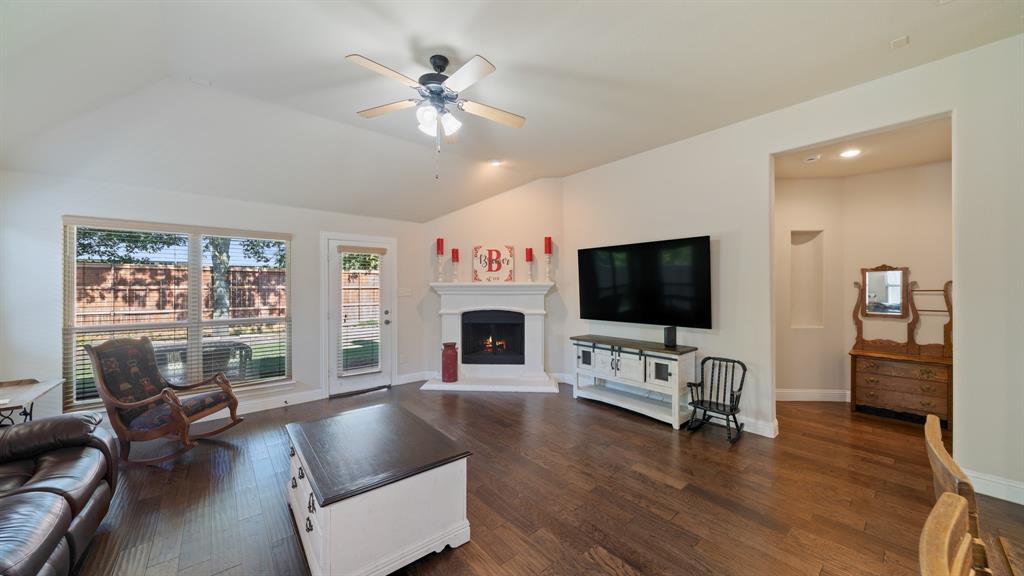 Vaulted ceilings, wood-finish flooring, corner fireplace with white mantle, and recessed wall niche