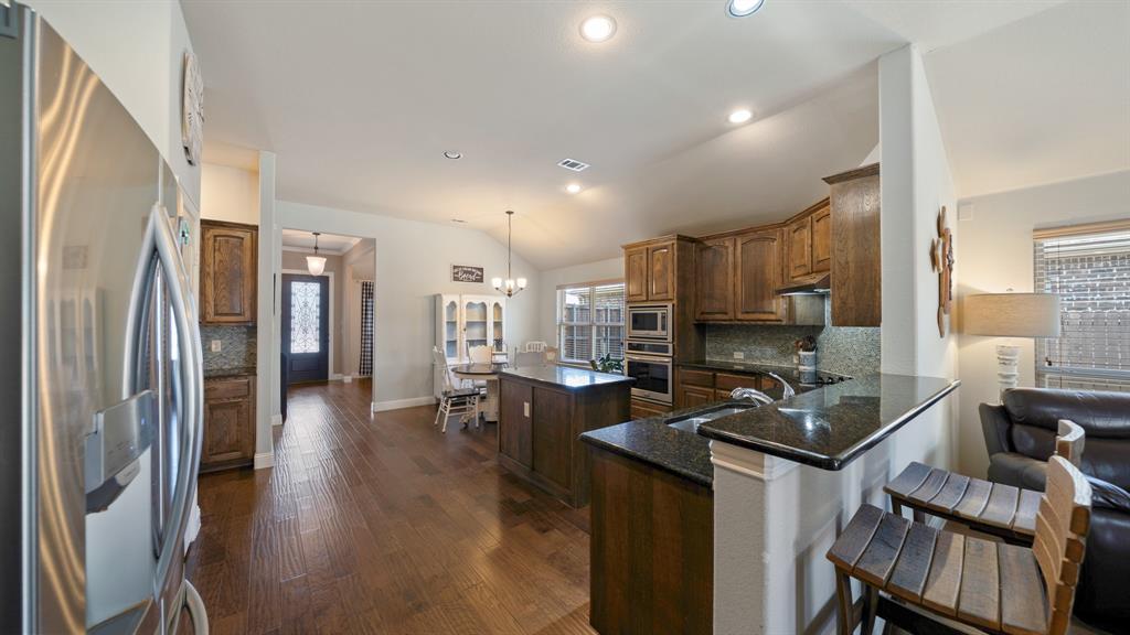 Kitchen featuring wood cabinetry, stone countertops, stainless steel appliances, a center island, and wood-finish flooring