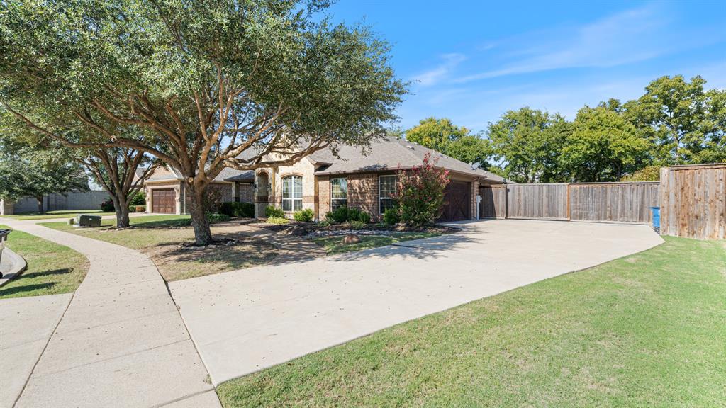 Single-story masonry exterior featuring a concrete driveway, a wood privacy fence, and mature trees on a landscaped lot Single-story masonry exterior featuring a concrete driveway, a wood privacy fence, and mature trees on a landscaped lot