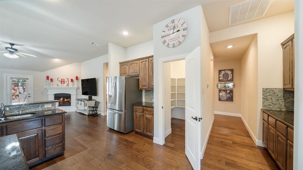 Kitchen featuring wood cabinetry, stone countertops, a walk-in pantry, and wood-finish flooring, complemented by a gas fireplace with a mantel