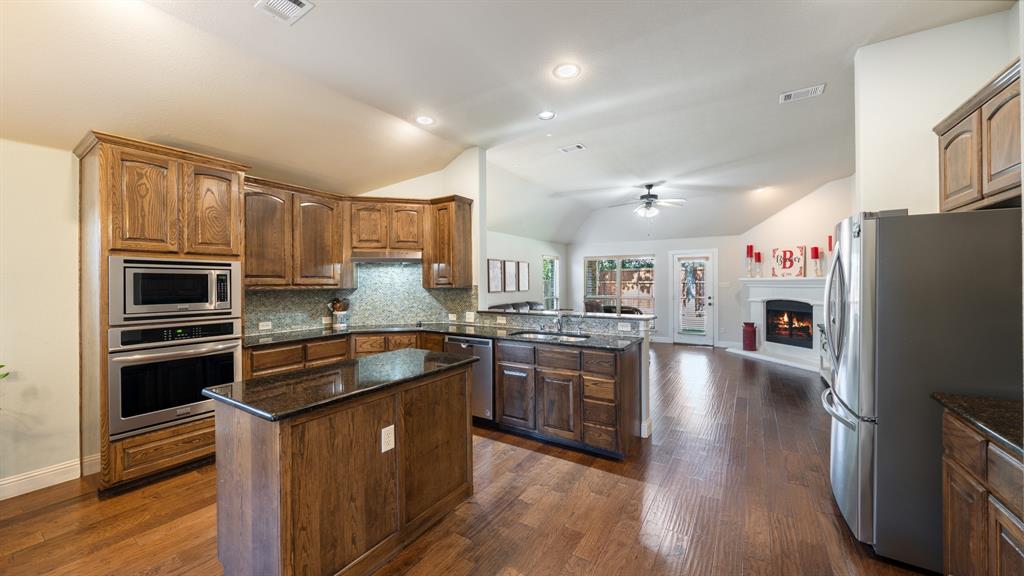 Kitchen featuring stained wood cabinetry, stone countertops, stainless steel wall-mounted oven and microwave, recessed lighting, and wood-finish flooring
