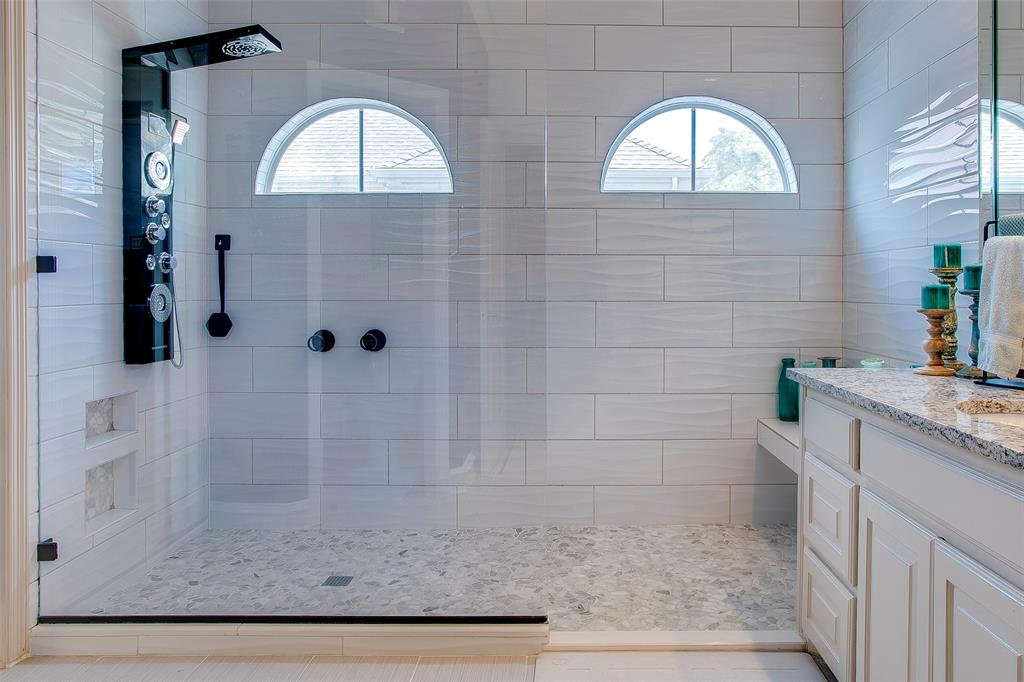 Glass-enclosed shower with a multi-function shower panel, integrated wall niches, and pebble-style floor tiling