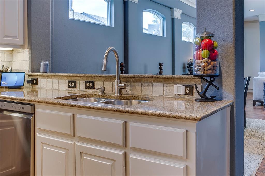 Kitchen featuring a double stainless steel sink with a gooseneck faucet, light granite countertops, white cabinetry with recessed panel doors, and a tiled backsplash