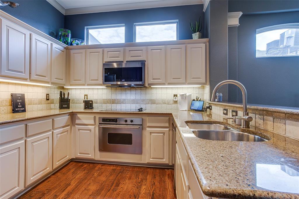 Kitchen featuring light-toned cabinetry, wood-finish flooring, undermount stainless steel double sink, built-in microwave, and an integrated oven