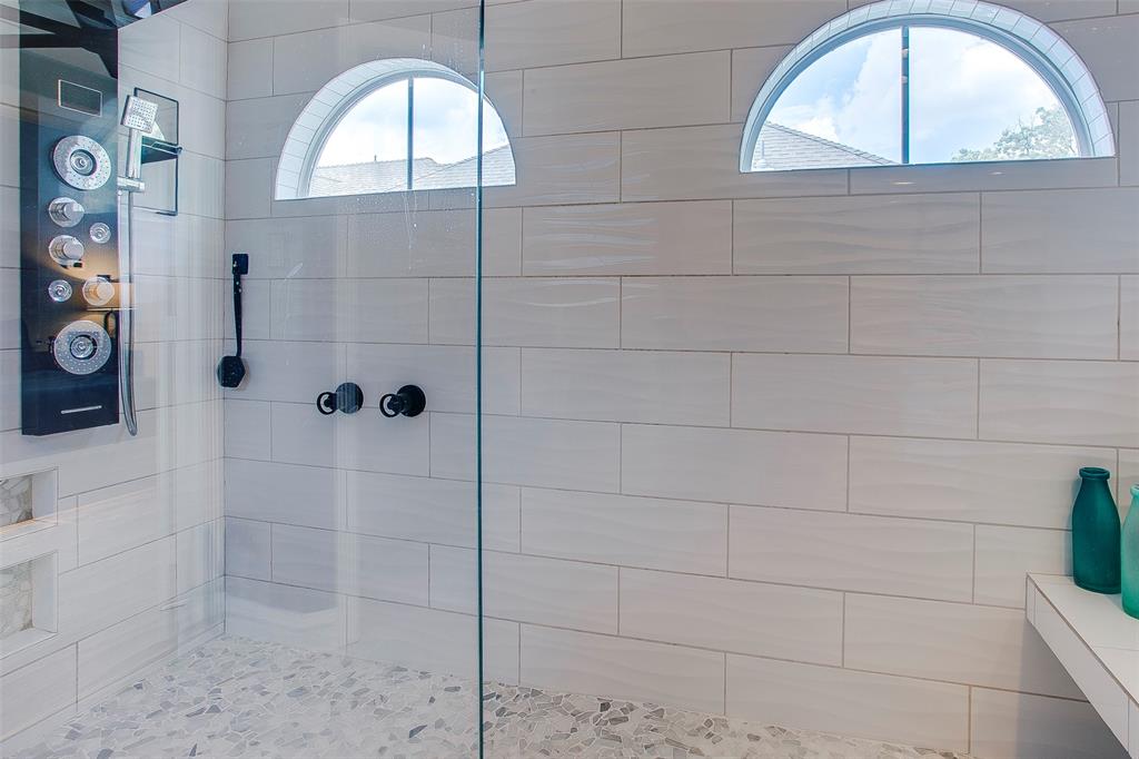 Glass-enclosed shower featuring a multi-function shower panel, two arched windows, a built-in bench, and pebble-tile flooring