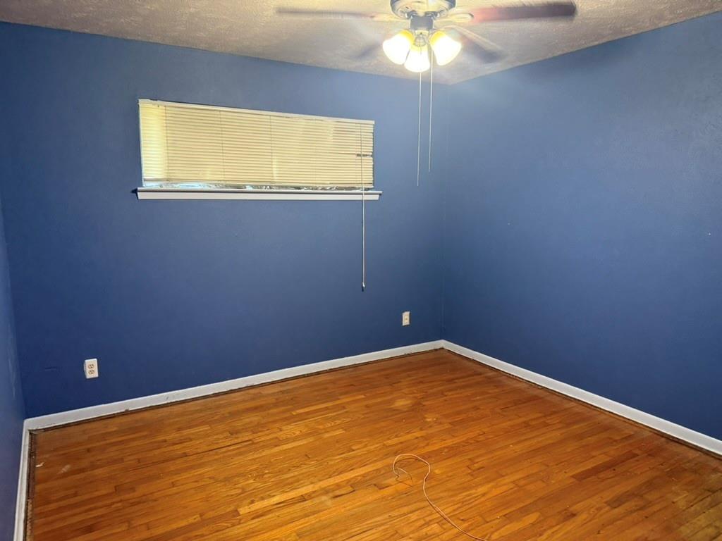 Room featuring wood-finish flooring, a ceiling-mounted light fixture with a fan, and a horizontal window with adjustable blinds