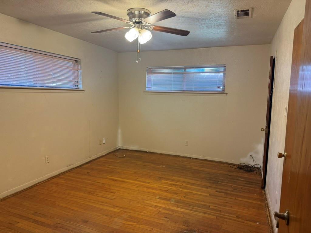 Room featuring wood-finish flooring, two windows with horizontal blinds, and a central ceiling fan with integrated lighting