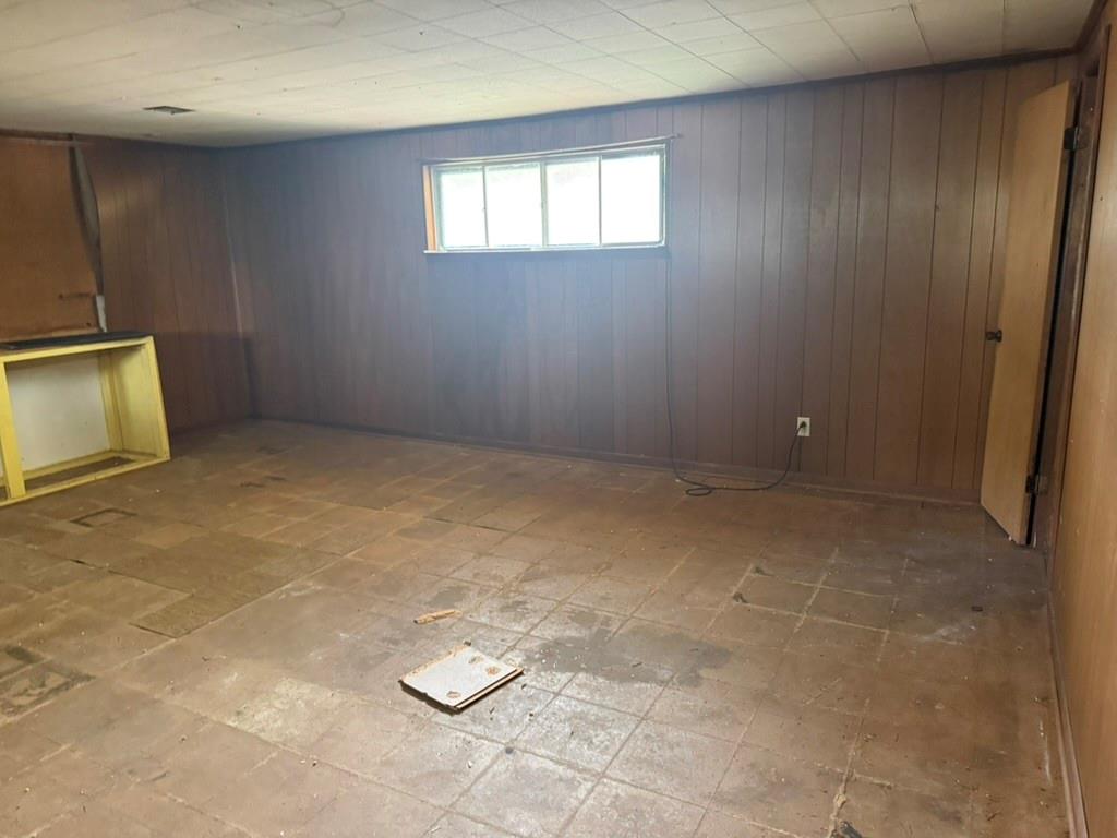 Room featuring wood-finish paneling, drop ceiling tiles, a sliding window, and tiled flooring