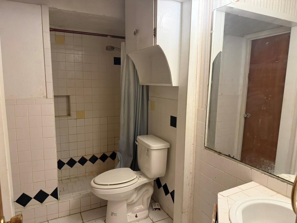 Bathroom featuring white tiled walls with decorative black accent tiling, a built-in shower stall, wall-mounted storage cabinetry, and a vanity mirror