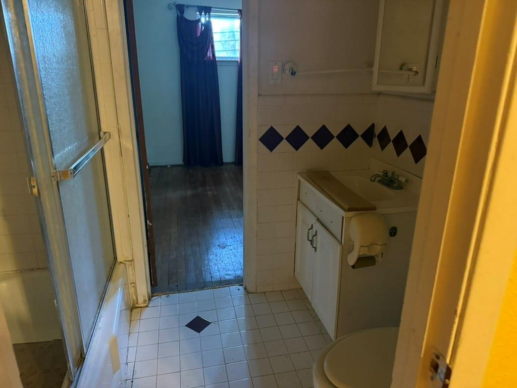 Bathroom featuring white tile flooring with inlaid decorative accents, a built-in vanity cabinet, and a shower-tub combination with glass enclosure