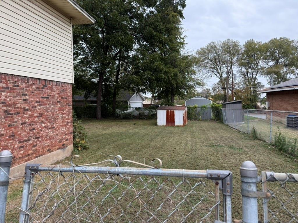 Rear yard featuring a brick and vinyl siding exterior, chain-link fencing, mature trees, and a detached storage structure