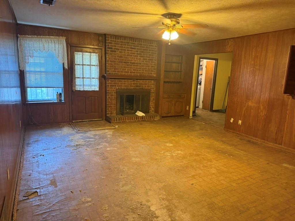 Interior room featuring wood-paneled walls, brick fireplace with a raised hearth, built-in cabinetry, and a ceiling fan with integrated light fixture