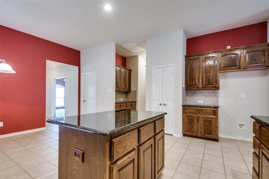 Kitchen featuring tasteful backsplash, baseboards, dark stone countertops, light tile patterned floors, and a center island