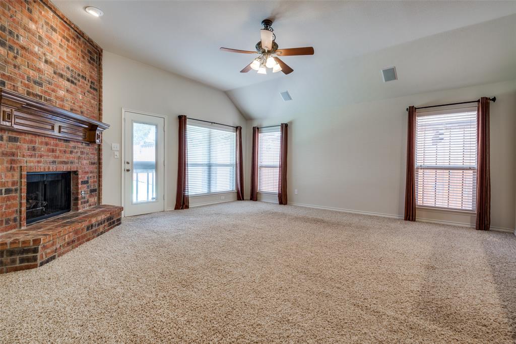 Unfurnished living room with visible vents, a brick fireplace, a ceiling fan, vaulted ceiling, and carpet flooring