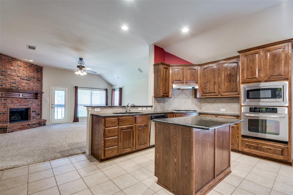 Kitchen with a sink, dark stone counters, vaulted ceiling, light colored carpet, and stainless steel appliances