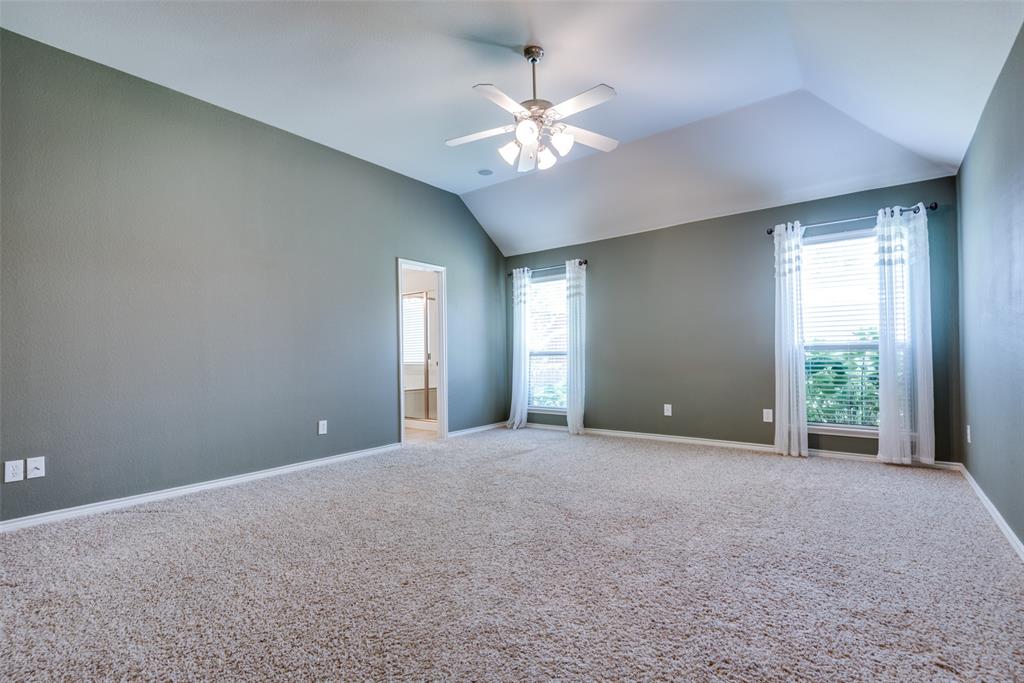 Carpeted spare room featuring a healthy amount of sunlight, ceiling fan, baseboards, and lofted ceiling