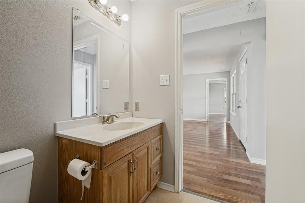 Bathroom featuring a wood-finish vanity with a rectangular sink, solid surface countertop, polished chrome faucet, and a large wall-mounted mirror with integrated lighting