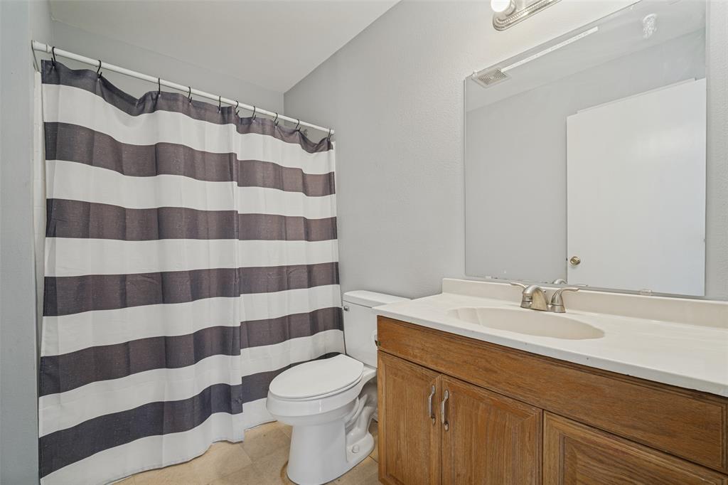 Bathroom featuring a wood-finish vanity with an integrated basin, a large wall-mounted mirror, overhead vanity lighting, and a bathtub with a curtain rod