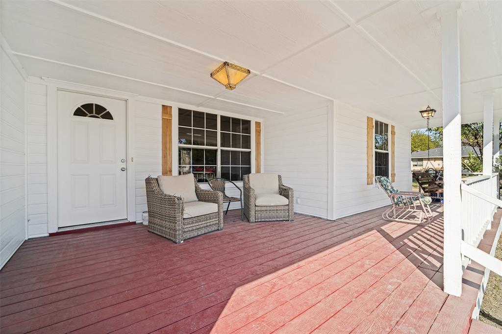 Covered front porch featuring wood-plank decking, white horizontal siding, decorative wood shutters, and dual flush-mount ceiling fixtures