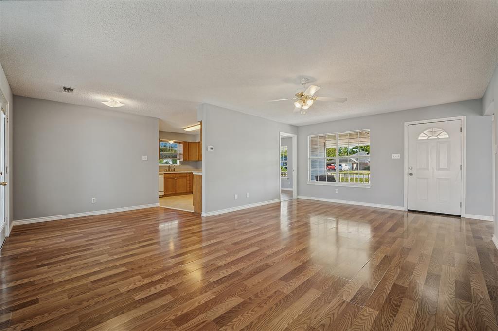 Open interior space featuring wood-finish flooring, a ceiling-mounted fan, multiple windows with grid detailing, and a paneled entry door