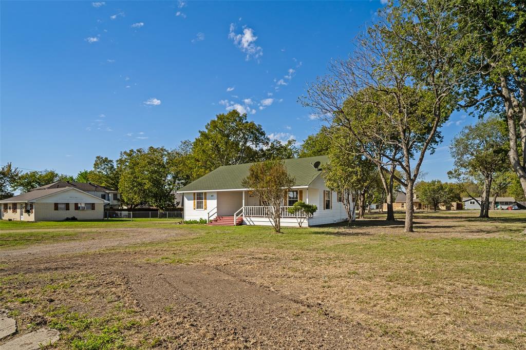 Single-story home featuring a covered front porch with white railing, exterior shutters, and a sloped roof set on a large lot with mature trees