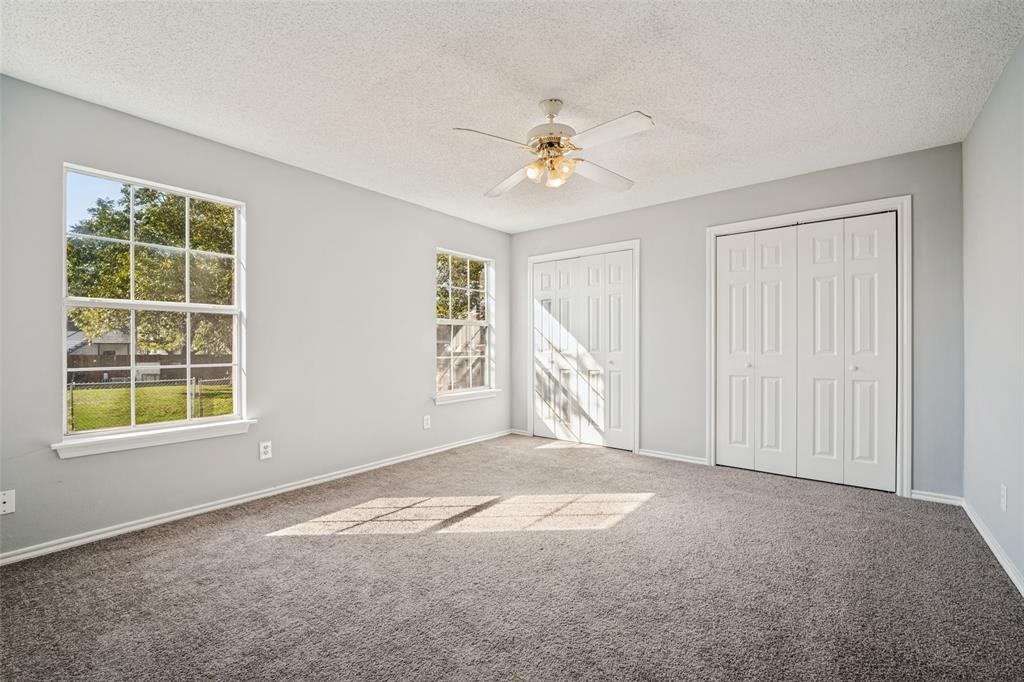 Neutral-toned interior featuring wall-to-wall carpeting, dual double-door closets, multiple pane windows, and a ceiling-mounted fan with integrated lighting