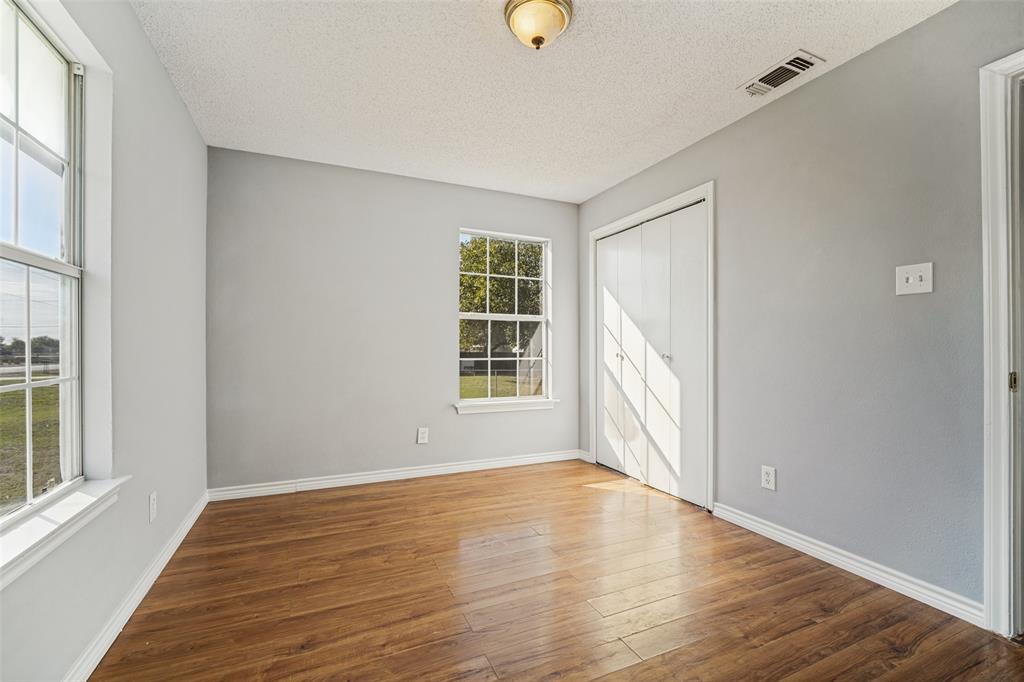 Room featuring wood-finish flooring, dual windows with grid detailing, neutral-toned wall paint, and a built-in closet with double doors Room featuring wood-finish flooring, dual windows with grid detailing, neutral-toned wall paint, and a built-in closet with double doors