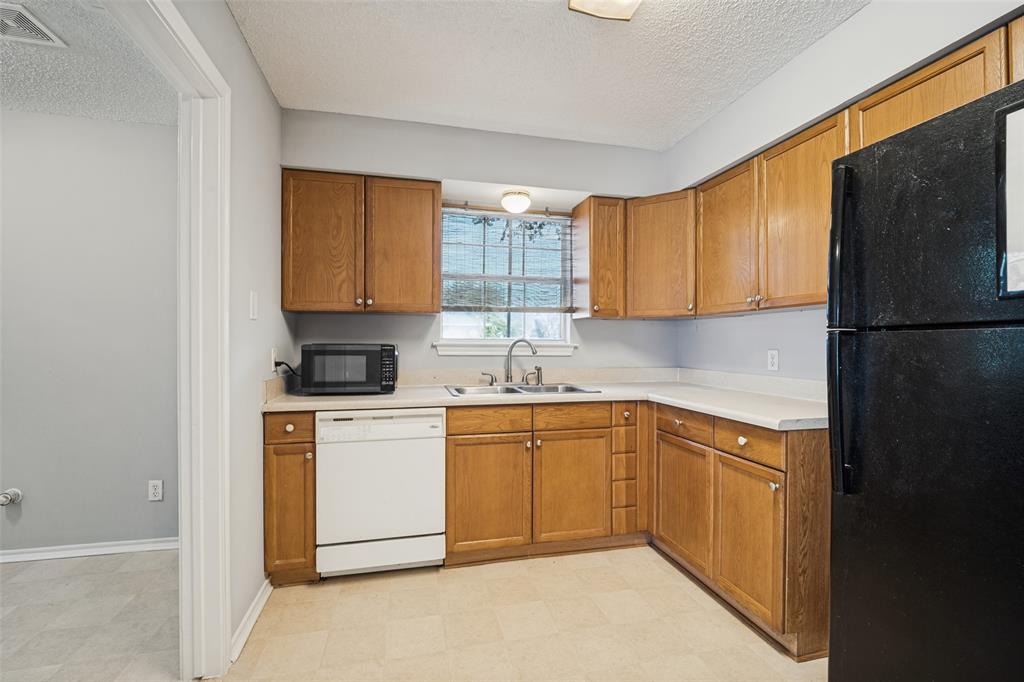 Kitchen featuring wood cabinetry, solid-surface countertops, dual-basin stainless steel sink, and light-toned tile flooring