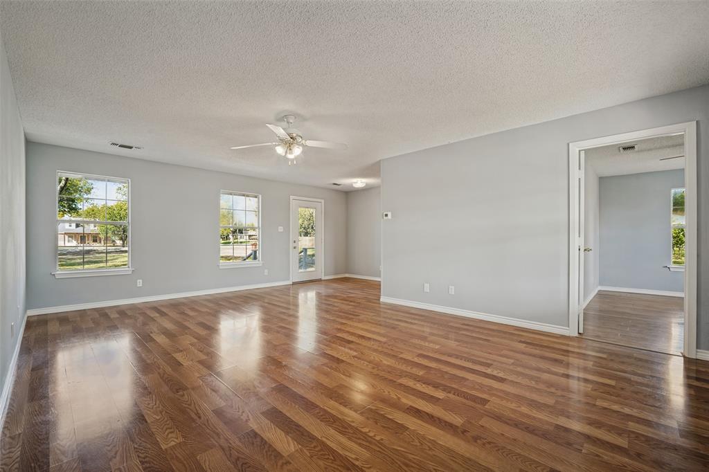 Open floor plan featuring wood-finish flooring, multi-pane windows, a central ceiling fan with integrated lighting, and a glass-paneled exterior door