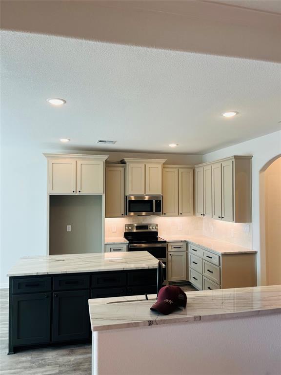 Kitchen featuring two-tone shaker-style cabinetry, stone countertops, central island, stainless steel range and microwave, and recessed lighting