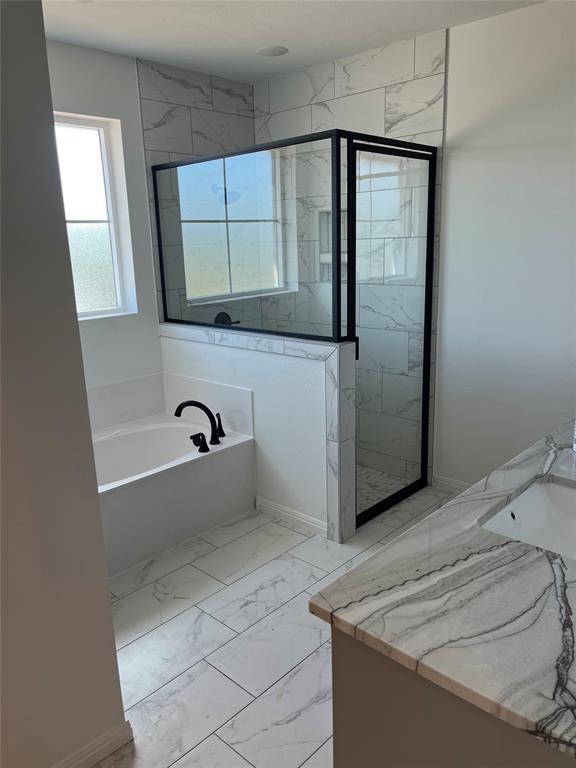 Bathroom featuring a soaking tub, glass-enclosed shower with matte black fixtures, stone-patterned tile flooring, and a stone countertop vanity