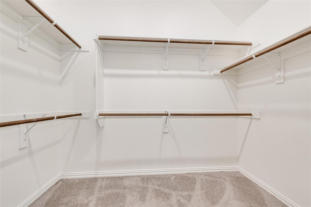 Walk-in closet featuring multi-level hanging rods, neutral carpeting, and white wall-mounted shelving units