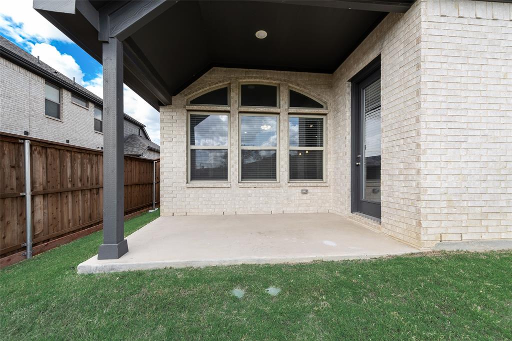 Covered concrete patio featuring a light-colored brick exterior, arched-top windows, and a wood privacy fence