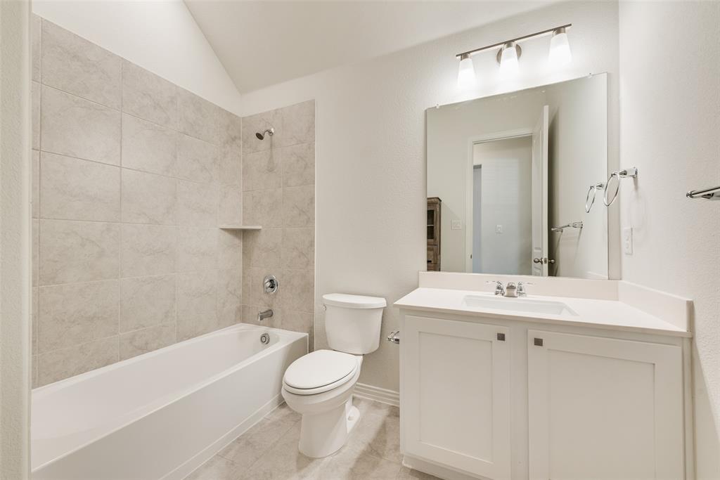 Full-width vanity with solid-surface countertop and integrated sink, large wall-mounted mirror, three-light fixture, and tiled tub-shower surround with built-in shelf