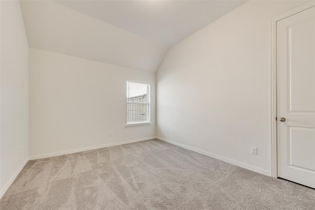 Neutral-toned carpeted flooring, vaulted ceiling, single-pane window with blinds, and a two-panel interior door
