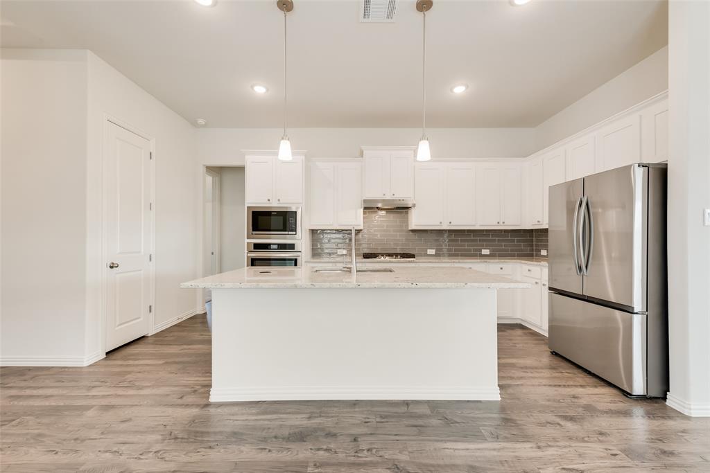 Kitchen featuring white cabinetry, stone-surface central island, subway tile backsplash, stainless steel appliances, and wood-finish flooring