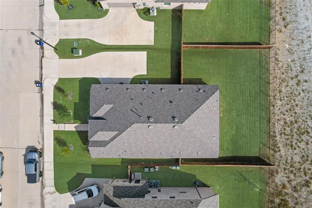 Aerial perspective featuring a multi-slope composite shingle roof, concrete driveway, and a fenced backyard with lawn