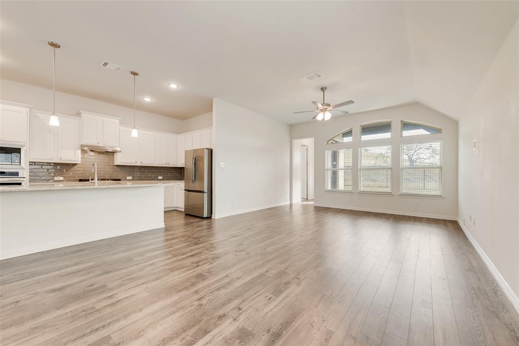 Open-concept interior featuring wood-finish flooring, vaulted ceilings, white cabinetry, stainless steel appliances, and arched windows