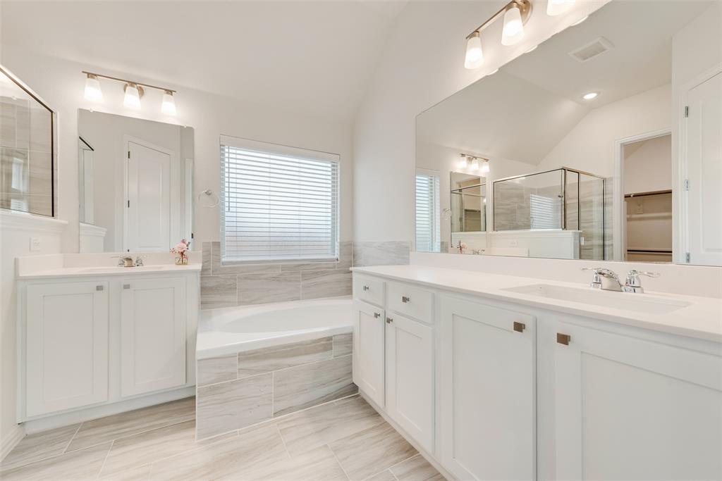 Dual white vanities with light-toned countertops, oversized wall-to-wall vanity mirrors, deep soaking tub with tile surround, and neutral large-format tile flooring